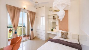 A hotel room with a bed, a chair, a balcony with curtains, a ceiling fan, and a bedside table with a mirror and a plant. - Prism by Red Olive4 Bhkomrecr Beaches it Park (Tirupporur)