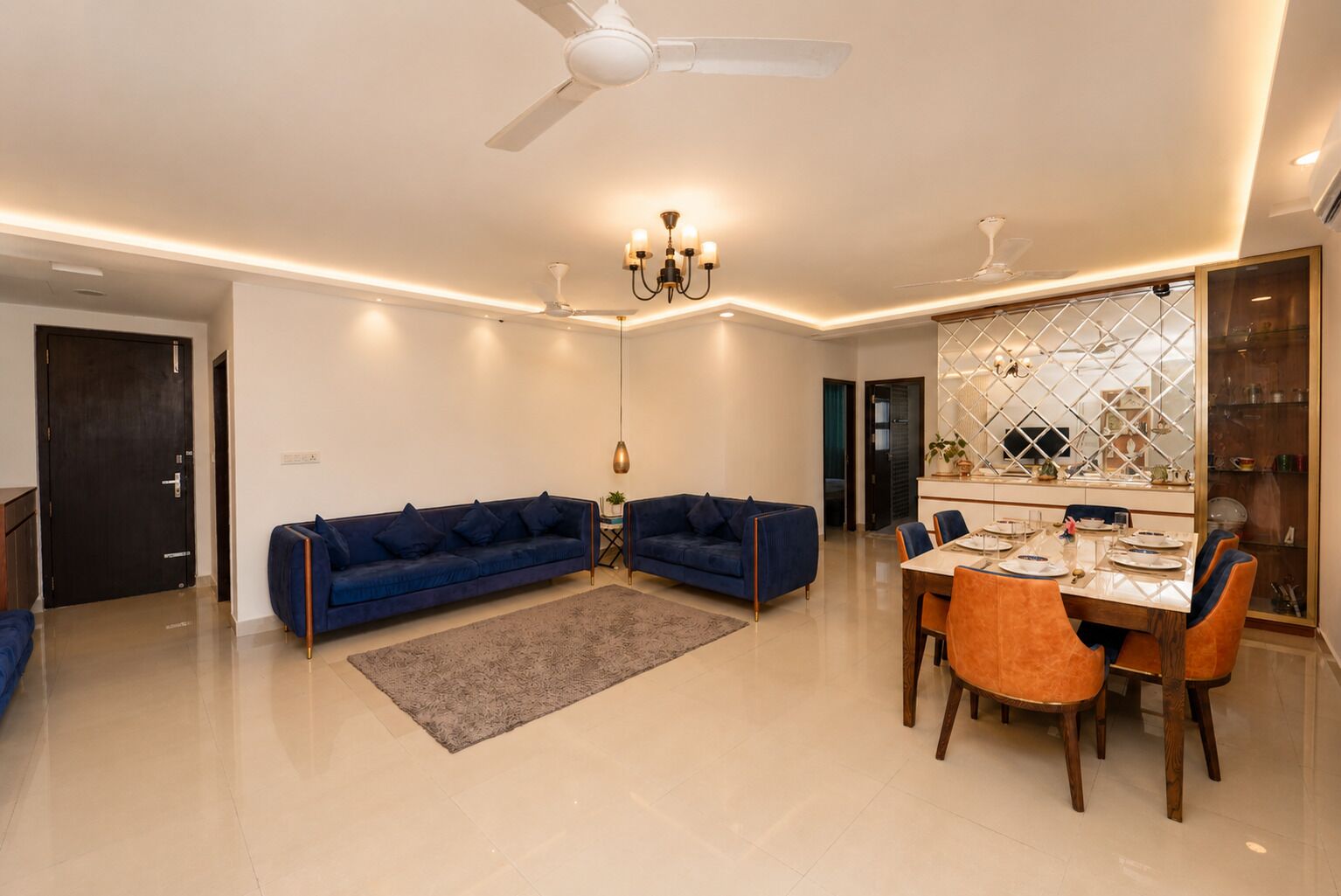 A modern living room with a sofa set, dining table, and chandelier.