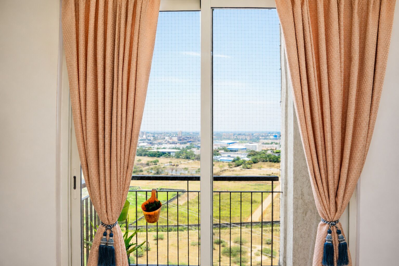 A balcony with a view of a cityscape, curtains, and a hanging plant.