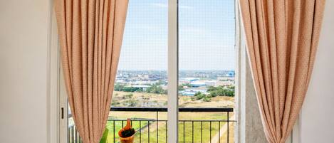 A balcony with a view of a cityscape, curtains, and a hanging plant.