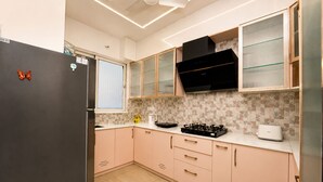 A kitchen with a refrigerator, stove, microwave, and cabinets. - Prism by Red Olive4 Bhkomrecr Beaches it Park (Tirupporur)