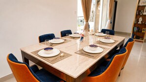 A dining table set for six with blue and orange chairs, a vase with flowers, and a bookshelf in the background. - Prism by Red Olive4 Bhkomrecr Beaches it Park (Tirupporur)