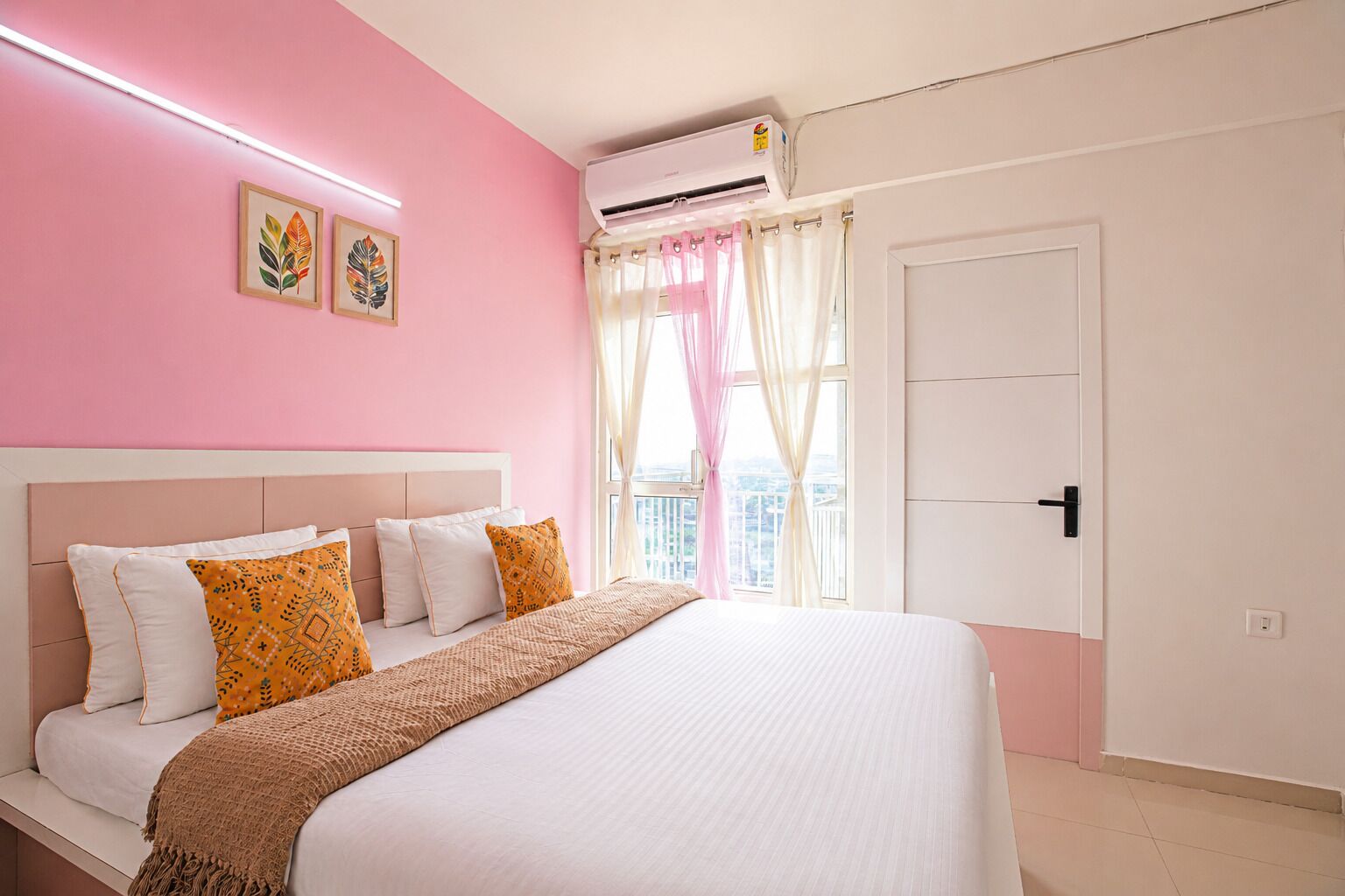 Un dormitorio con cama, almohadas, una ventana con cortinas, un equipo de aire acondicionado y una puerta.