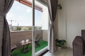 A balcony with a view of construction cranes, a wooden chair, a small table with two white mugs, and a potted plant. - Ember by Red Olive 2bhk 5min Itpl Whitefield (Bengaluru)