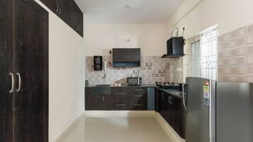 A kitchen with dark cabinets, a microwave, a refrigerator, and a tiled backsplash.