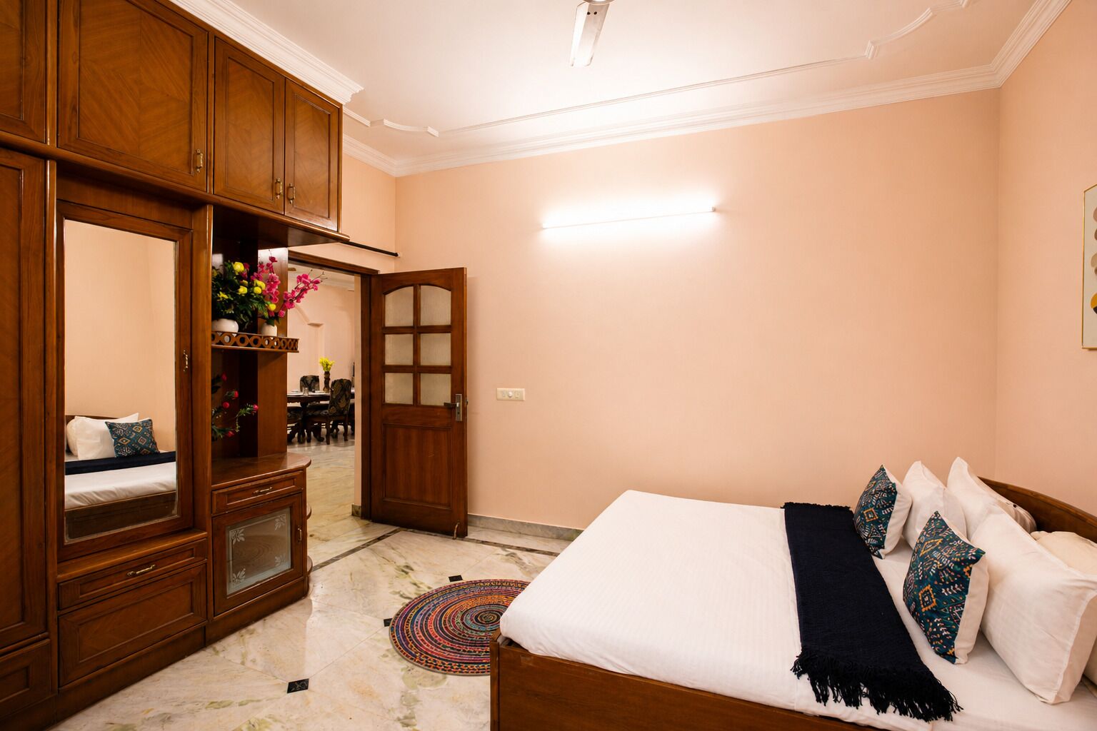 A bedroom with a bed, a wardrobe, a mirror, and a dining area visible through an open door.