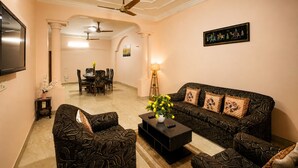 Ein Wohnzimmer mit Sofa, Sesseln, Couchtisch, Fernseher, Essbereich mit Stühlen und Tisch sowie Deckenventilator.