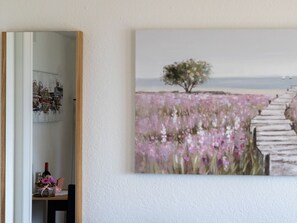A room with a painting of a field and a tree, a wooden door, and a small table with a bottle and flowers. - Schwyz, (Schwyz), by Interhome (Seewen SZ)