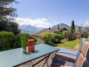 Une terrasse avec une table et des chaises, entourée de verdure et offrant une vue sur les montagnes.