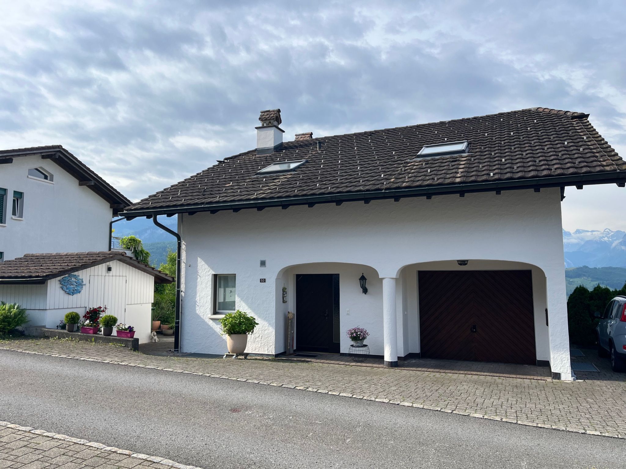 Ein zweistöckiges Haus mit einem Ziegeldach, einem Hauseingang mit einer dunklen Tür und einem kleinen Balkon mit einem Blumentopf.