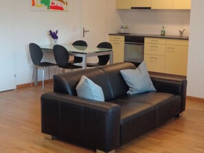 Un salon moderne avec un canapé en cuir noir, une table à manger en verre et des chaises.
