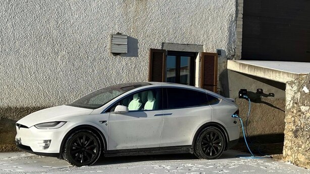 En vit bil parkerad framför en byggnad med en strukturerad fasad, ett fönster och en dörr.