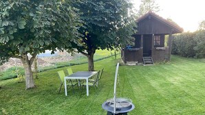 Ett grönområde med enklare utemöbler, bestående av ett bord och stolar, en grill och en träkonstruktion.