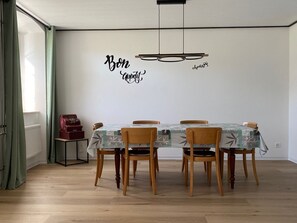 Zona pranzo con tavolo imbandito per quattro persone, sedie di legno, una radio d'epoca e una parete con frasi motivazionali.
