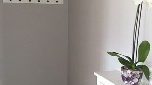 A bathroom with a white cabinet, a wicker stool, a shelf with a basket, and a potted plant with white flowers. - Appartement - Serena, (Courtetelle), by Interhome (Courtételle)