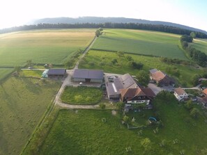 A rural property with multiple buildings, including a large house with a sloped roof, a barn, and several smaller structures. There is a fenced area with a solar panel array, and the property is surrounded by expansive fields. - Appartement - Serena, (Courtetelle), by Interhome (Courtételle)