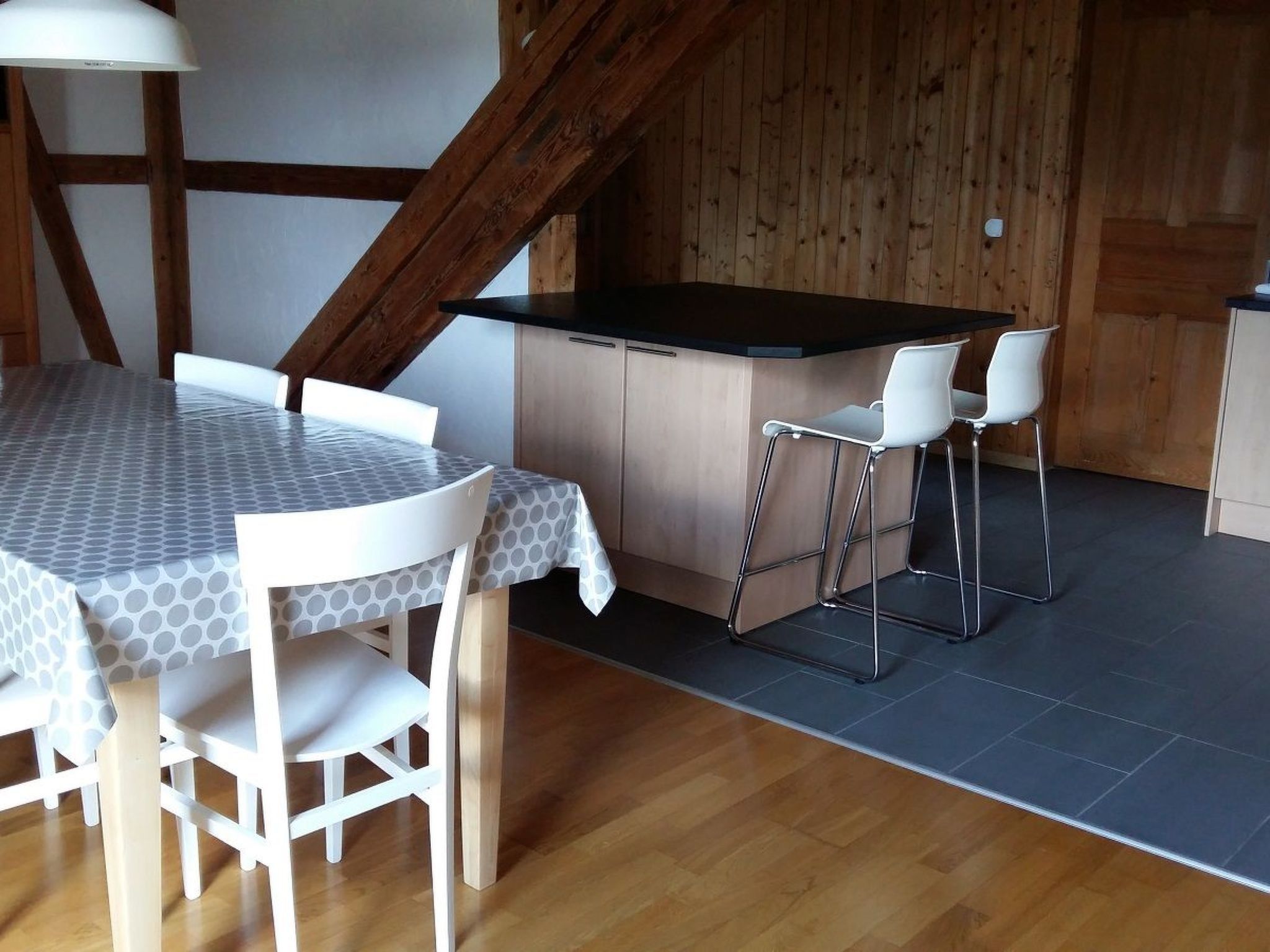 A dining area with a round table and chairs, a kitchen with a bar area, and wooden beams on the ceiling.