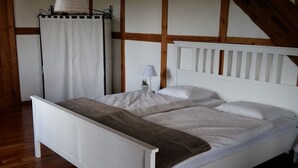 A white bed with a wooden headboard, a bedside lamp, and a window with a curtain. - Appartement - Serena, (Courtetelle), by Interhome (Courtételle)