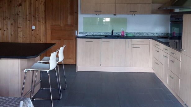 A modern kitchen with wooden cabinets, a black countertop, and two white bar stools. - Appartement - Serena, (Courtetelle), by Interhome (Courtételle)