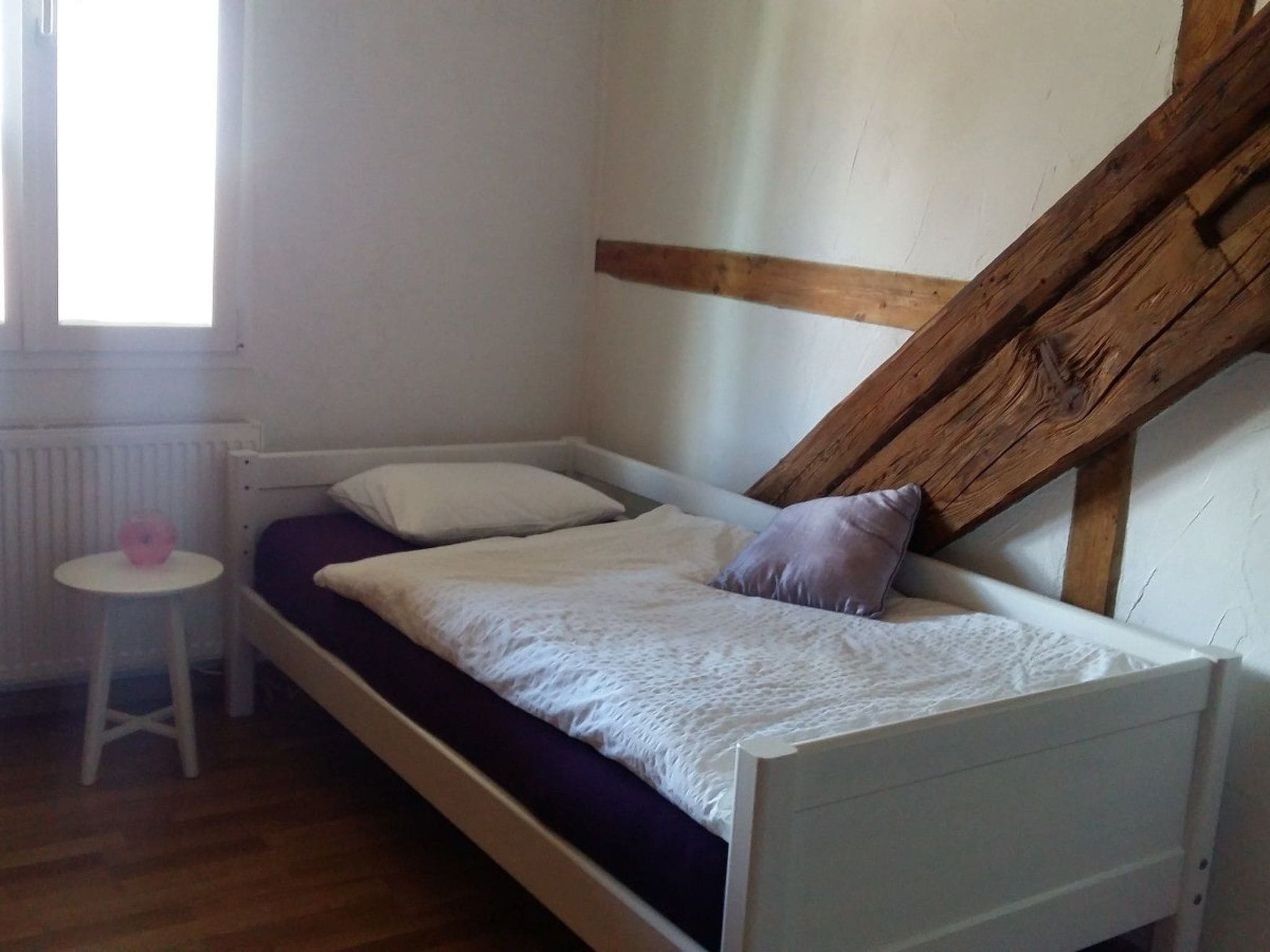 A small, single-bed room with a slanted ceiling, a radiator, a small table, and a window.