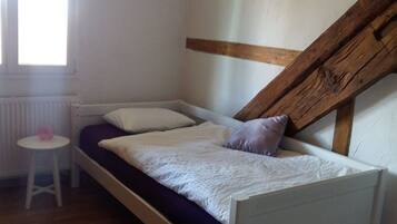 A small, single-bed room with a slanted ceiling, a radiator, a small table, and a window.