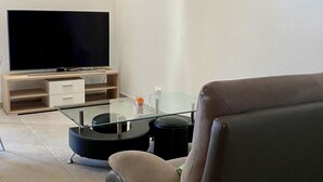 A modern living room with a flat-screen TV, a glass coffee table, a sofa, and a painting on the wall. - Gîte - Le Cras, (Soubey), by Interhome (Soubey)