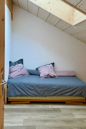 A small, cozy room with a sloped ceiling, a bed with a patterned bedspread, and two pillows. - Gîte - Le Cras, (Soubey), by Interhome (Soubey)