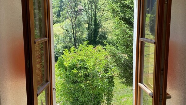 A room with a large window offering a view of a lush green landscape. - Gîte - Le Cras, (Soubey), by Interhome (Soubey)