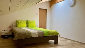 A bedroom with a bed, a nightstand, a wooden door, and a light fixture on the wall. - Gîte - Le Cras, (Soubey), by Interhome (Soubey)