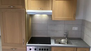 A compact kitchen with wooden cabinets, a built-in oven, a stovetop, and a sink. - Gîte - Le Cras, (Soubey), by Interhome (Soubey)