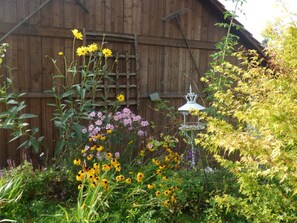 Un jardín con diversas flores y una estructura de madera al fondo.