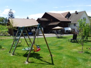 A residential area with a swing set, a lawn, a house with a tiled roof, and outdoor seating. - Studio - Le Râtelier, (Coeuve), by Interhome (Coeuve)