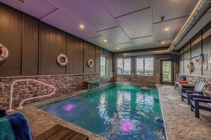 An indoor swimming pool with stone walls, a lifebuoy, and a view of the outdoors. - 4 King Suites | Indoor Pool + Mtn Views (Sevierville)