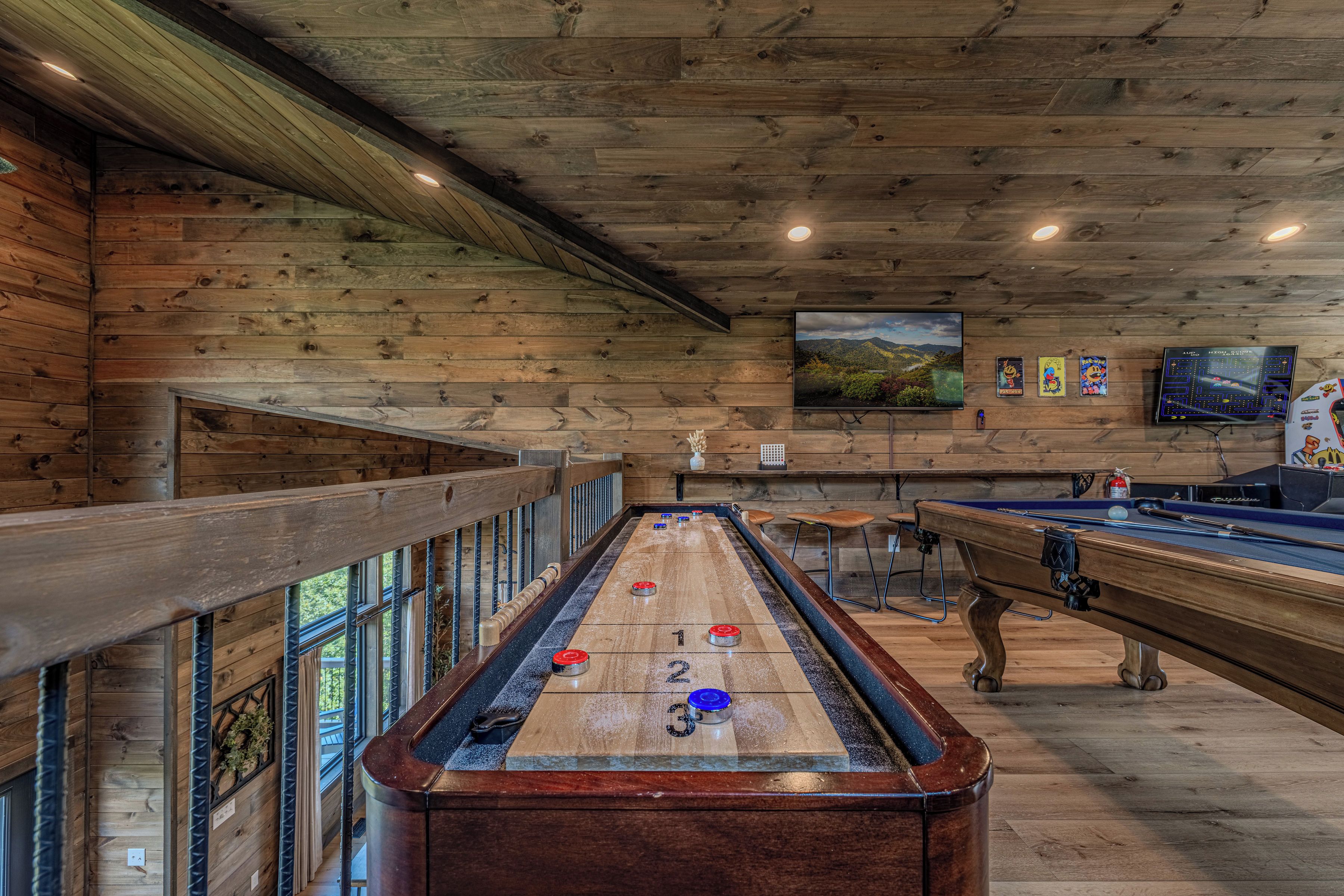 A pool table with shuffleboard pucks, a billiards table, and a television mounted on the wall.