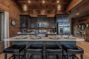 A modern kitchen with a central island, bar stools, and wooden paneling. - 4 King Suites | Indoor Pool + Mtn Views (Sevierville)