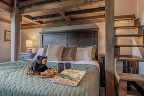 A bedroom with a bed, a wooden headboard, a teddy bear, a book, and a nightstand with a lamp. - 4 King Suites | Indoor Pool + Mtn Views (Sevierville)
