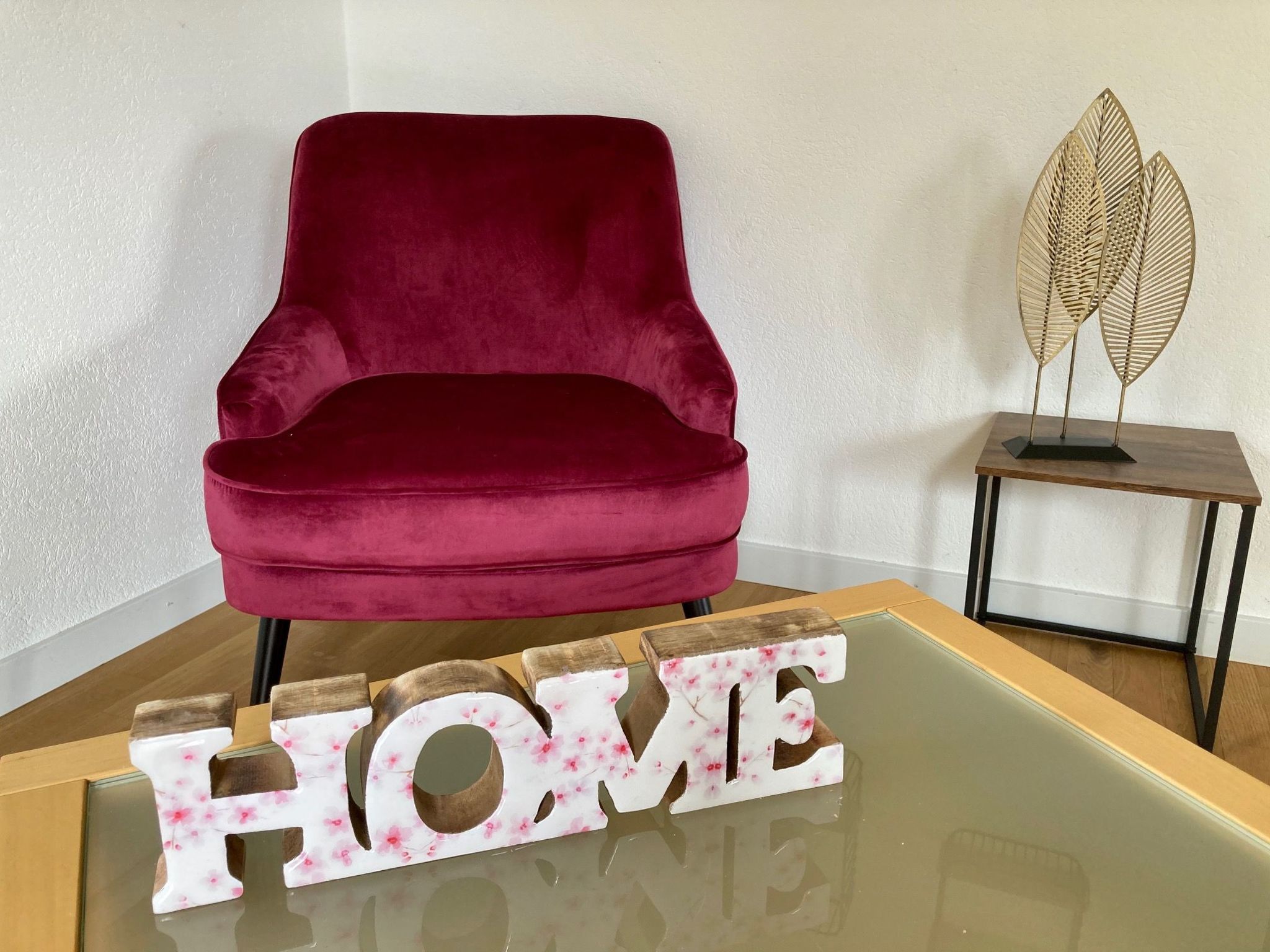 Un fauteuil en velours rouge, un panneau décoratif en forme de chiffre « 5 », et une sculpture en forme de feuille posée sur une table.