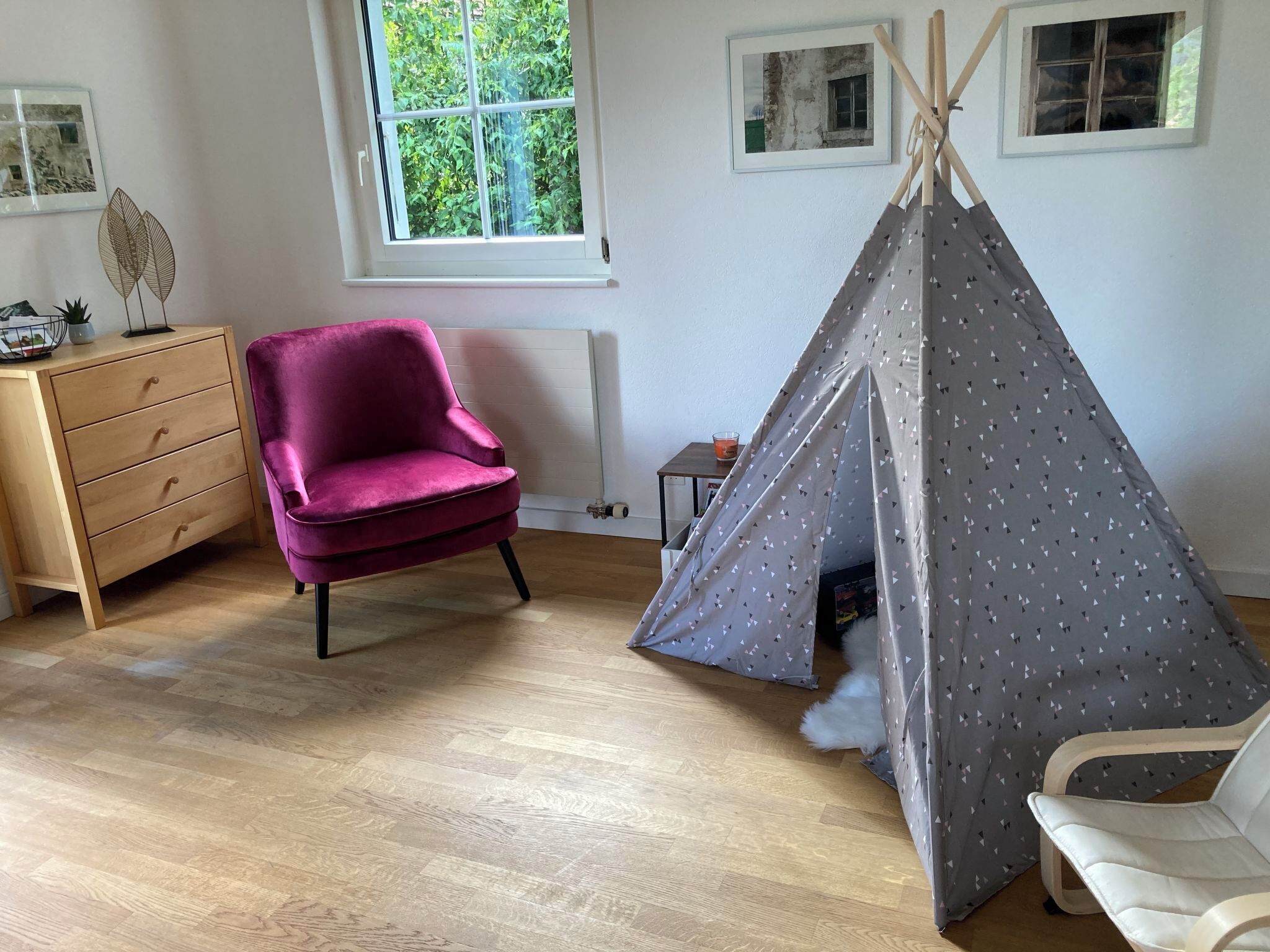 Ein Zimmer mit Holzboden, einem violetten Stuhl, einem weißen Stuhl, einem kleinen Tisch mit Kerze und einem Tipizelt.