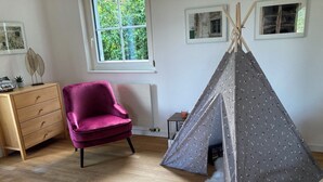 Et værelse med trægulv, en lilla stol, en hvid stol, et lille bord med et lys og en tipi-telt.