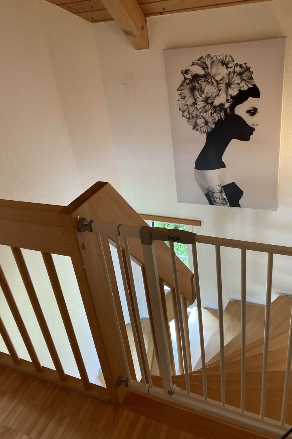 Un escalier en bois avec une rampe, menant à une pièce dont le mur est blanc et qui est décorée d’une œuvre d’art encadrée représentant un motif floral.