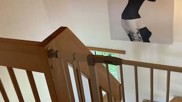 Un escalier en bois avec une rampe, menant à une pièce dont le mur est blanc et qui est décorée d’une œuvre d’art encadrée représentant un motif floral.