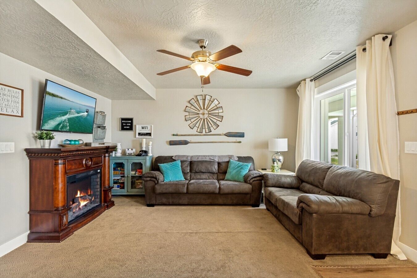 A living room with a fireplace, a ceiling fan, a television, and a large window with curtains.