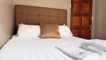 A hotel room with a large bed, a wooden door, and a neatly made bed with white linens and a brown pillow.