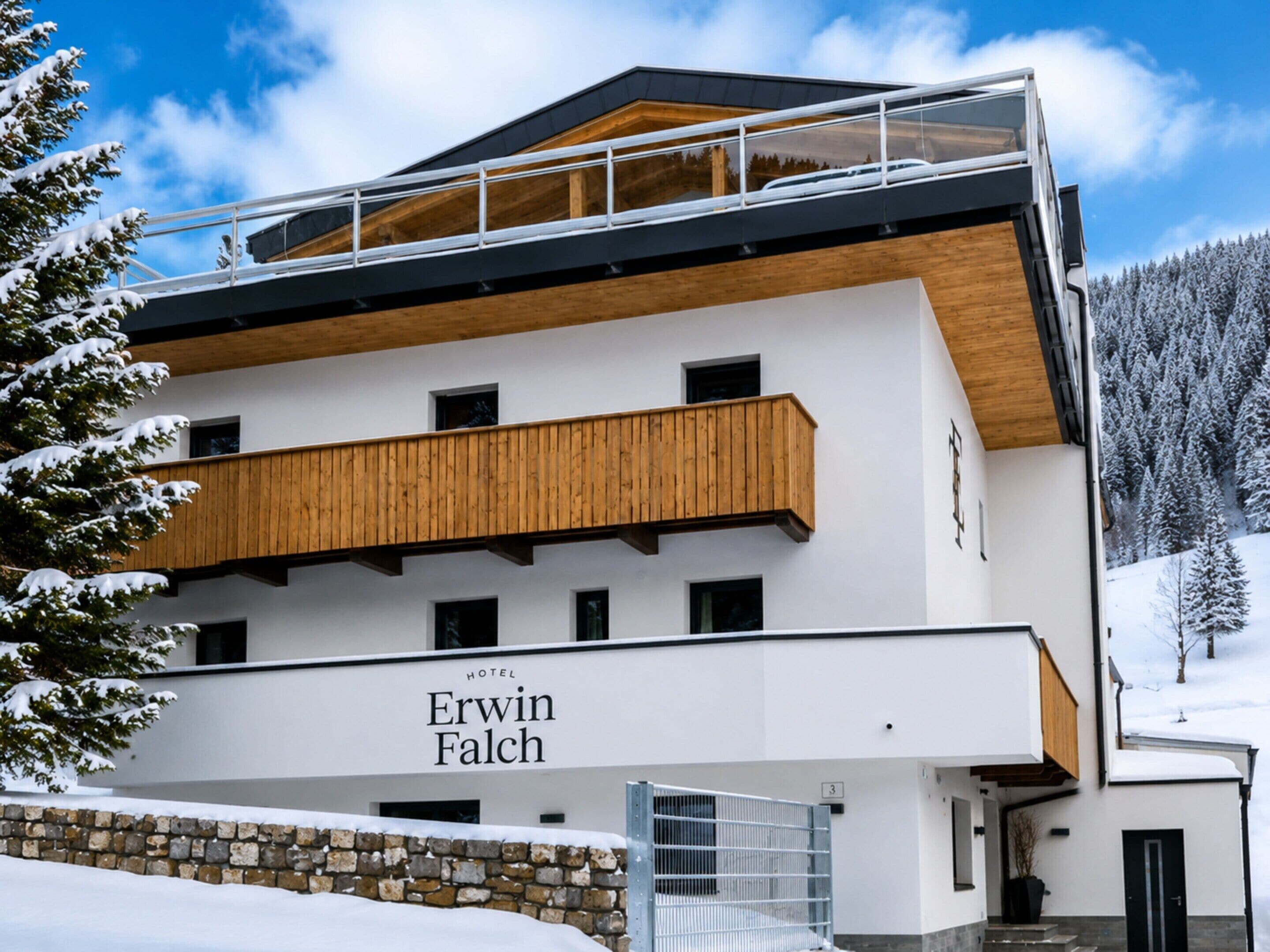 Ein modernes Hotel mit einem Holzbalkon, einer Steinwand und einem Schild mit der Aufschrift 'Erwin Falch'.