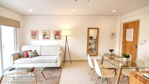 A modern living room with a sofa, coffee table, dining table, and chairs. There are framed pictures on the wall, a floor lamp, and a mirror. - Corporate Stays Edificio Pilar - N2A2 (Asunción)