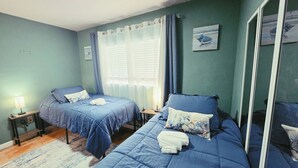 Ein Schlafzimmer mit zwei Betten, einem Fenster mit Vorhängen, einem Nachttisch mit Lampe und einem Spiegel.