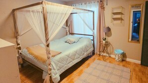 Ein Einzelbett mit Baldachin, ein Nachttisch mit Lampe, ein kleiner Hocker und ein an der Wand befestigtes Regal.