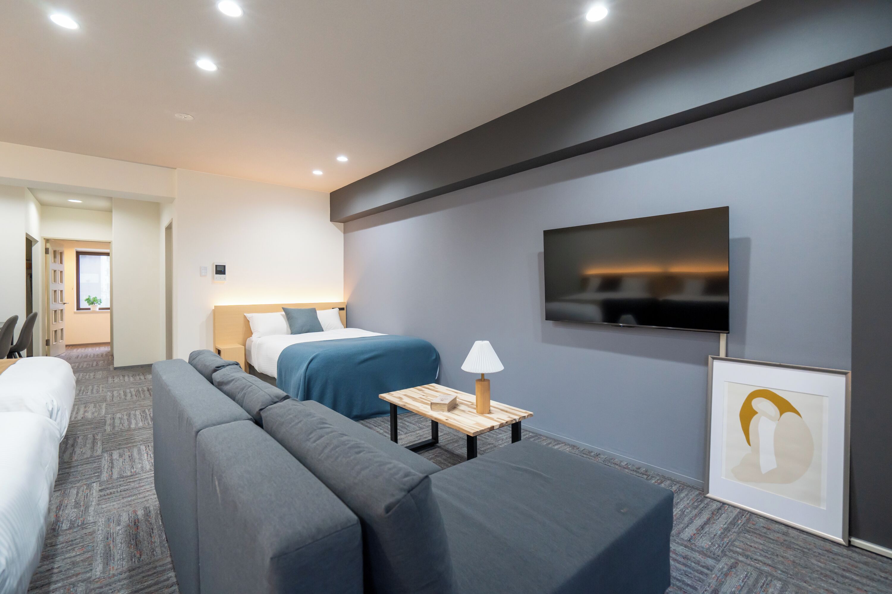 Habitación de hotel con sofá, cama, televisor y una pequeña mesa con lámpara.