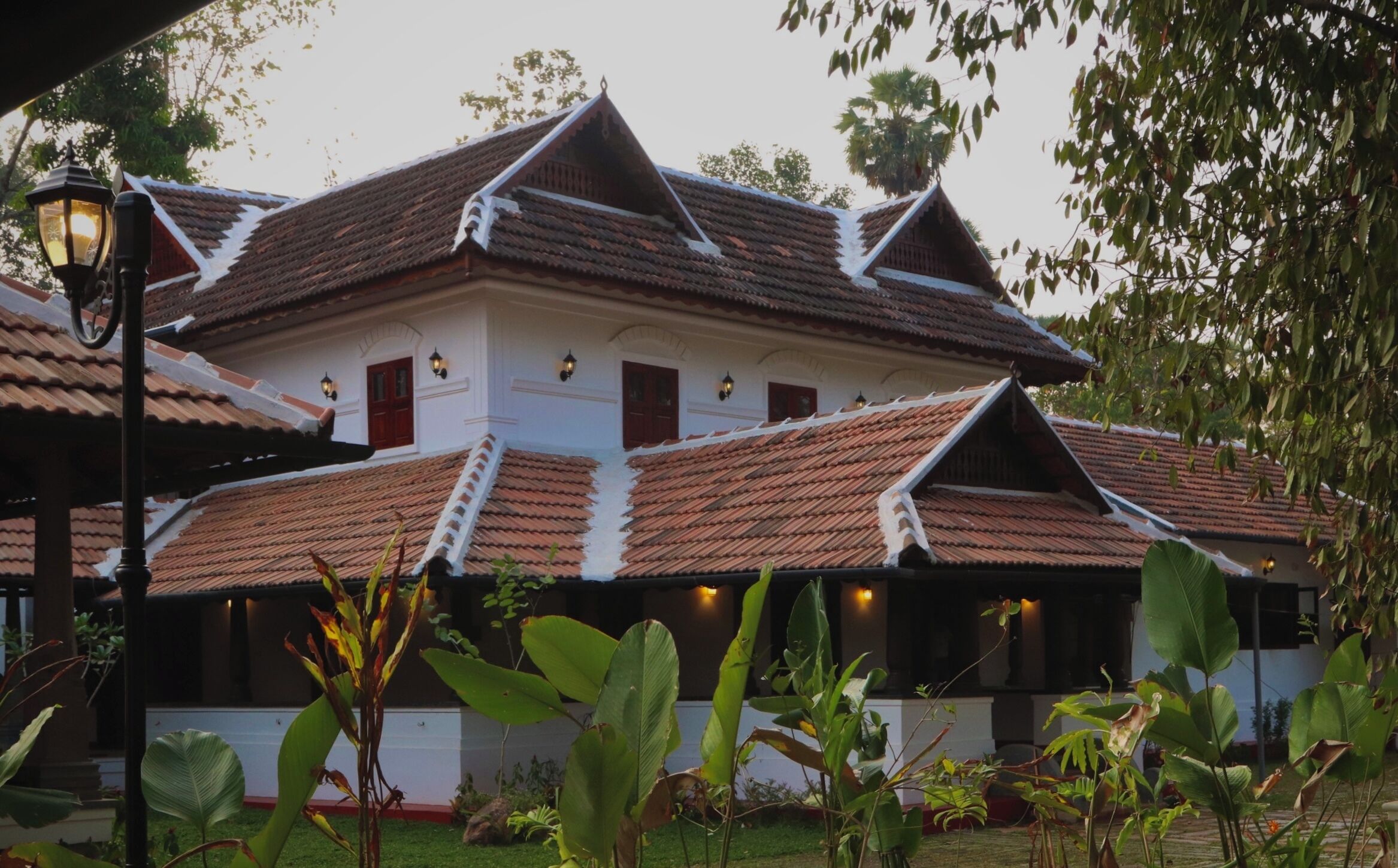 A traditional building with a tiled roof, multiple windows, and a well-maintained garden with large leafy plants.