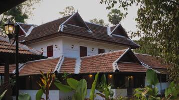 A traditional building with a tiled roof, multiple windows, and a well-maintained garden with large leafy plants.